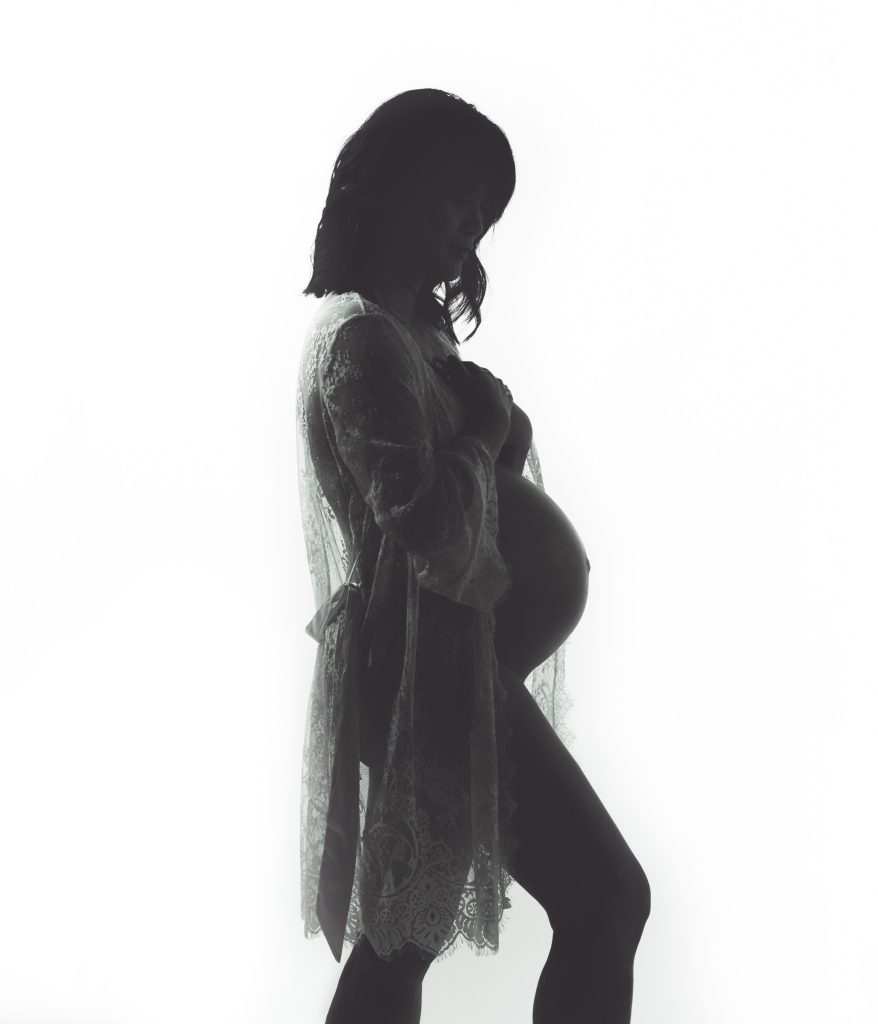 Backlit maternity silhouette of a pregnant woman wearing a lace robe