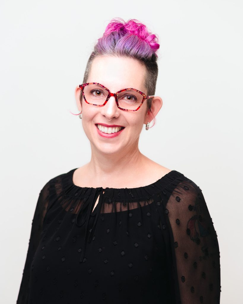 Creative professional headshot of a woman with pink hair and red glasses