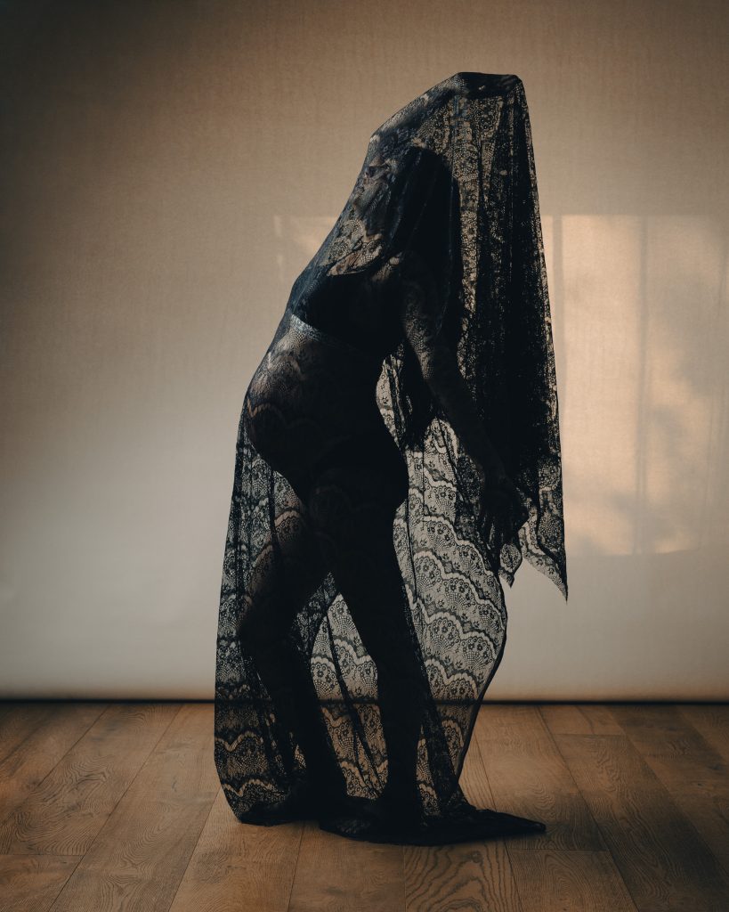 Creative studio maternity portrait using dramatic black lace fabric