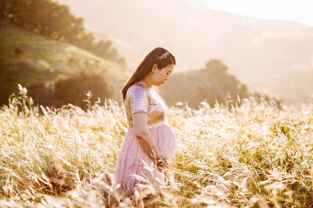 Expectant mother in a pink dress photographed outdoors in a sunlit field