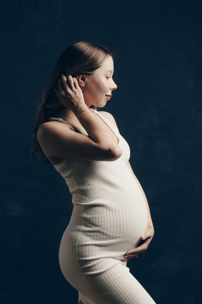 Side-profile studio portrait of an expectant mother in a fitted dress