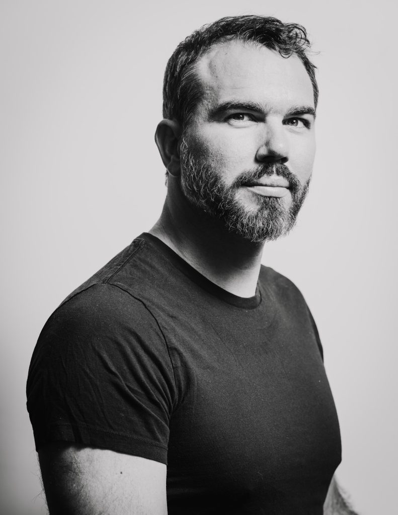 Black and white professional headshot of a bearded man