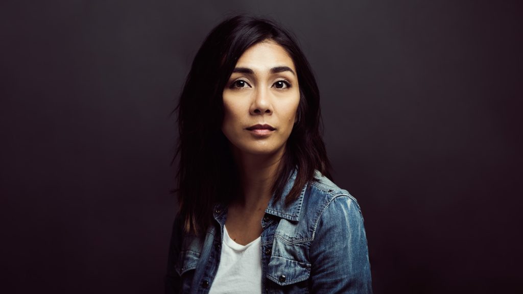 Professional portrait of a woman wearing a denim jacket against a dark background