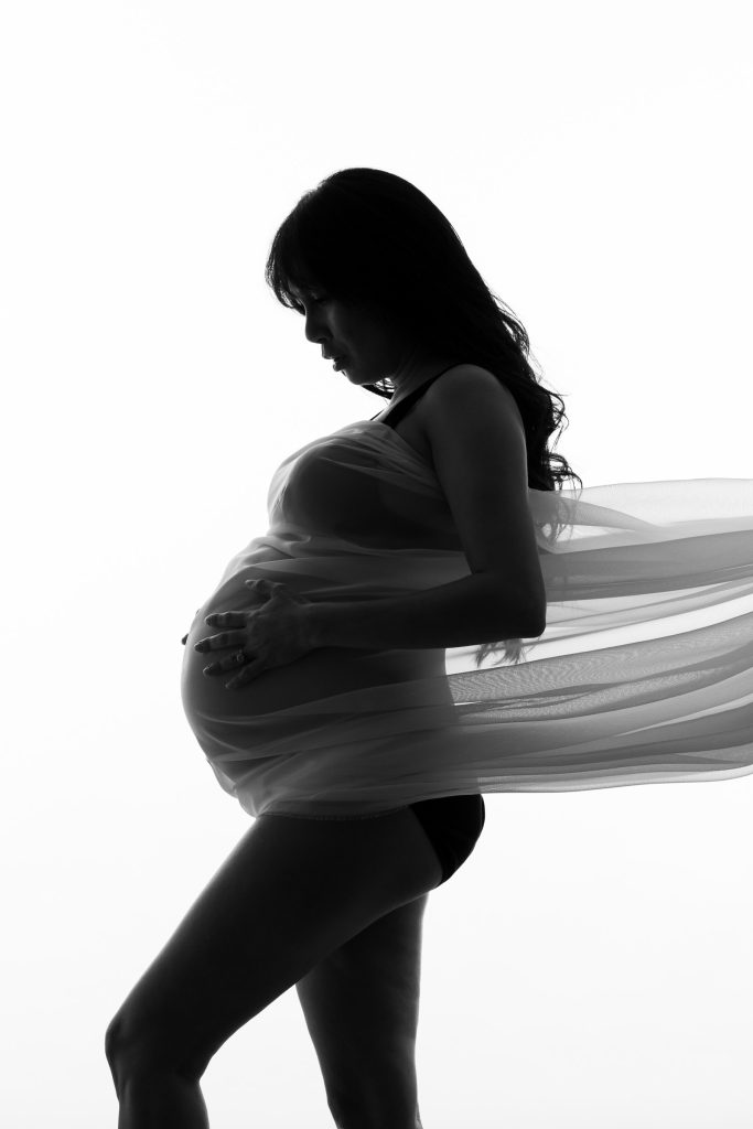 Silhouette maternity portrait of a pregnant woman wrapped in flowing fabric